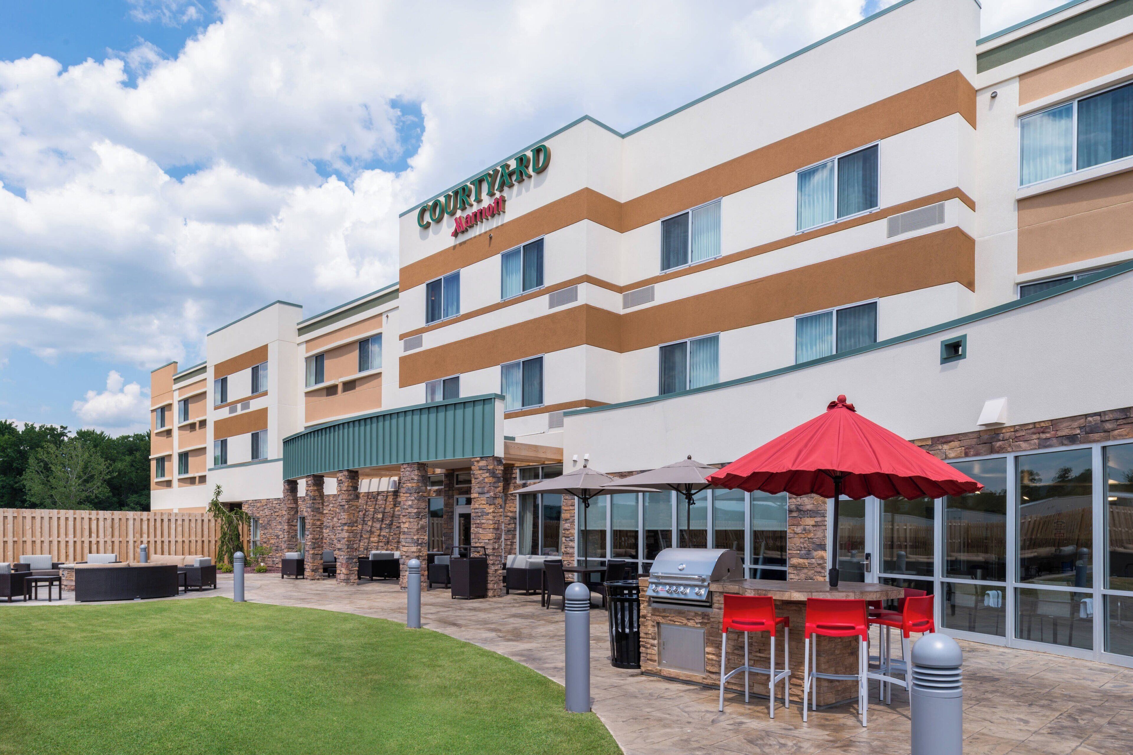 Un hotel Courtyard by Marriott con mesas al aire libre, zona de barbacoa y césped cuidado.