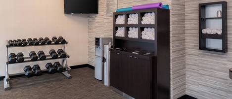 A fitness center with dumbbells, a water dispenser, a scale, and a TV on the wall.
