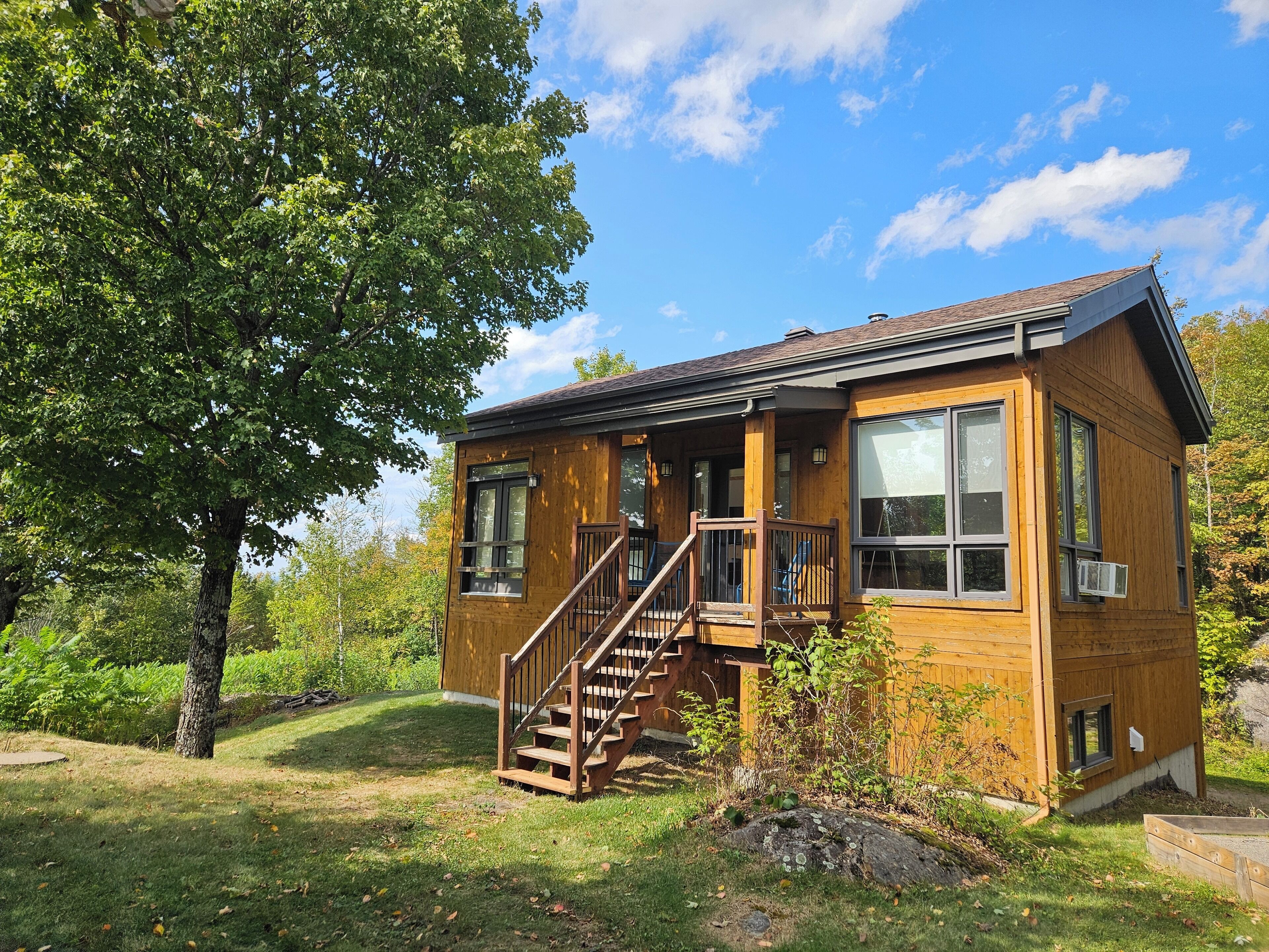 A wooden cabin with a porch, a staircase, and large windows.