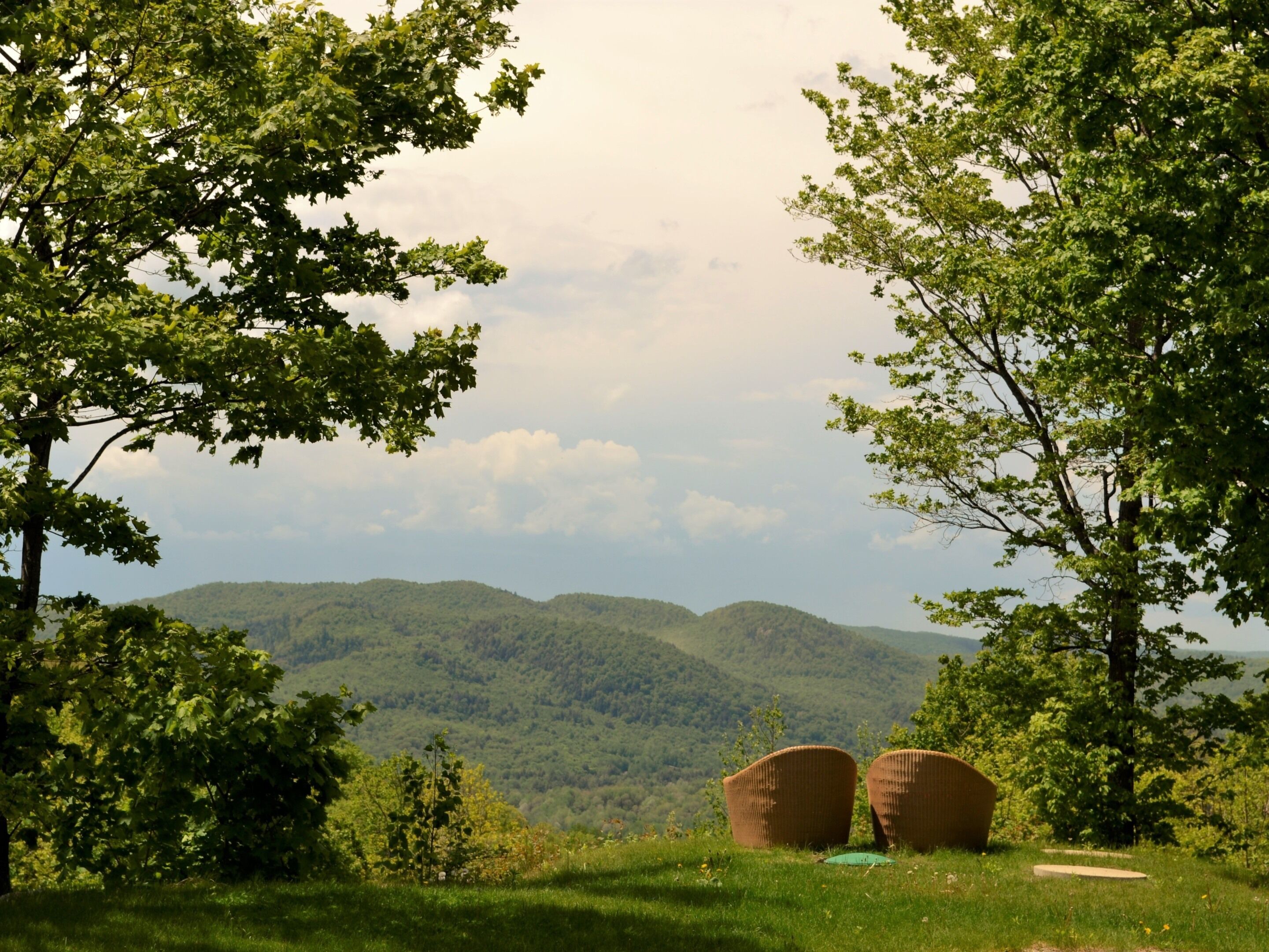 Paesaggio naturale con una zona erbosa, due sedie in vimini e vista su dolci colline lontane.