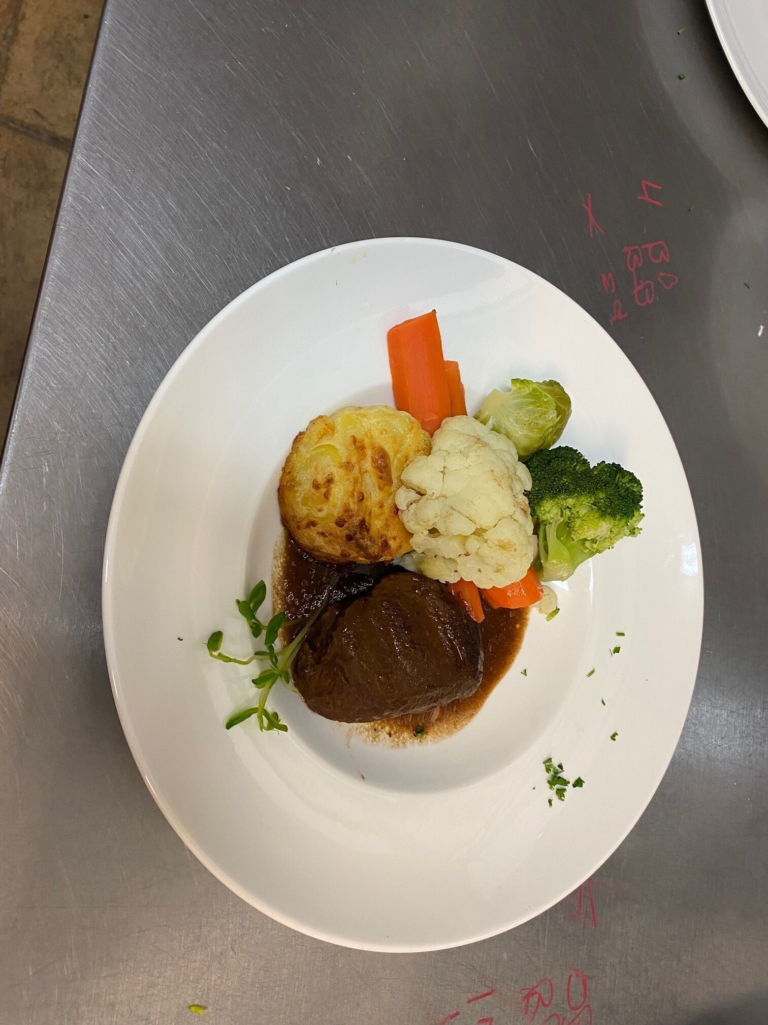 A white plate with a piece of meat, mashed potatoes, carrots, cauliflower, and broccoli.