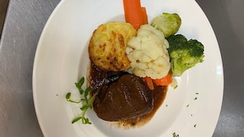 A white plate with a piece of meat, mashed potatoes, carrots, cauliflower, and broccoli.