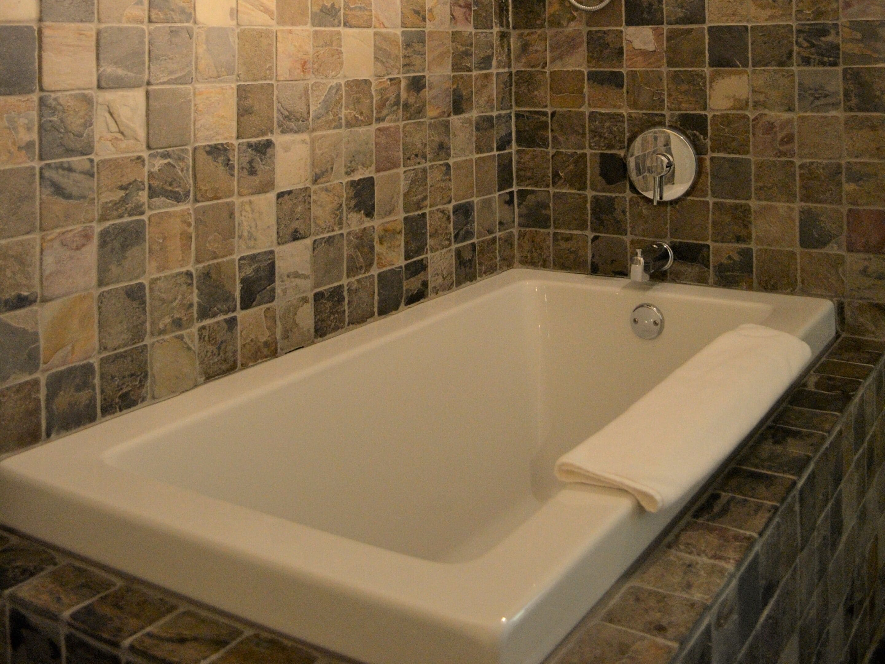 Una bañera rectangular con interior blanco, frente a una pared de mosaicos.