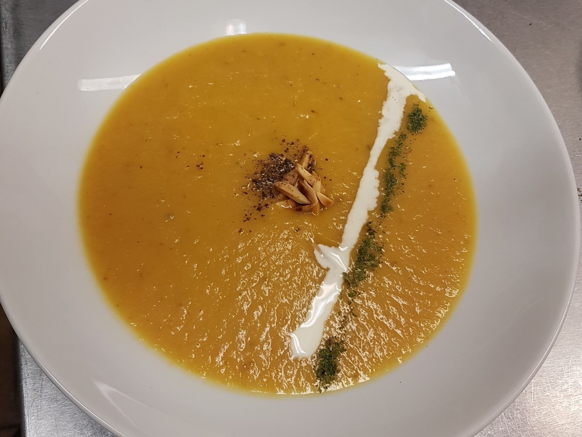 Une assiette blanche contenant une soupe crémeuse, garnie d’herbes et agrémentée d’un filet de crème.