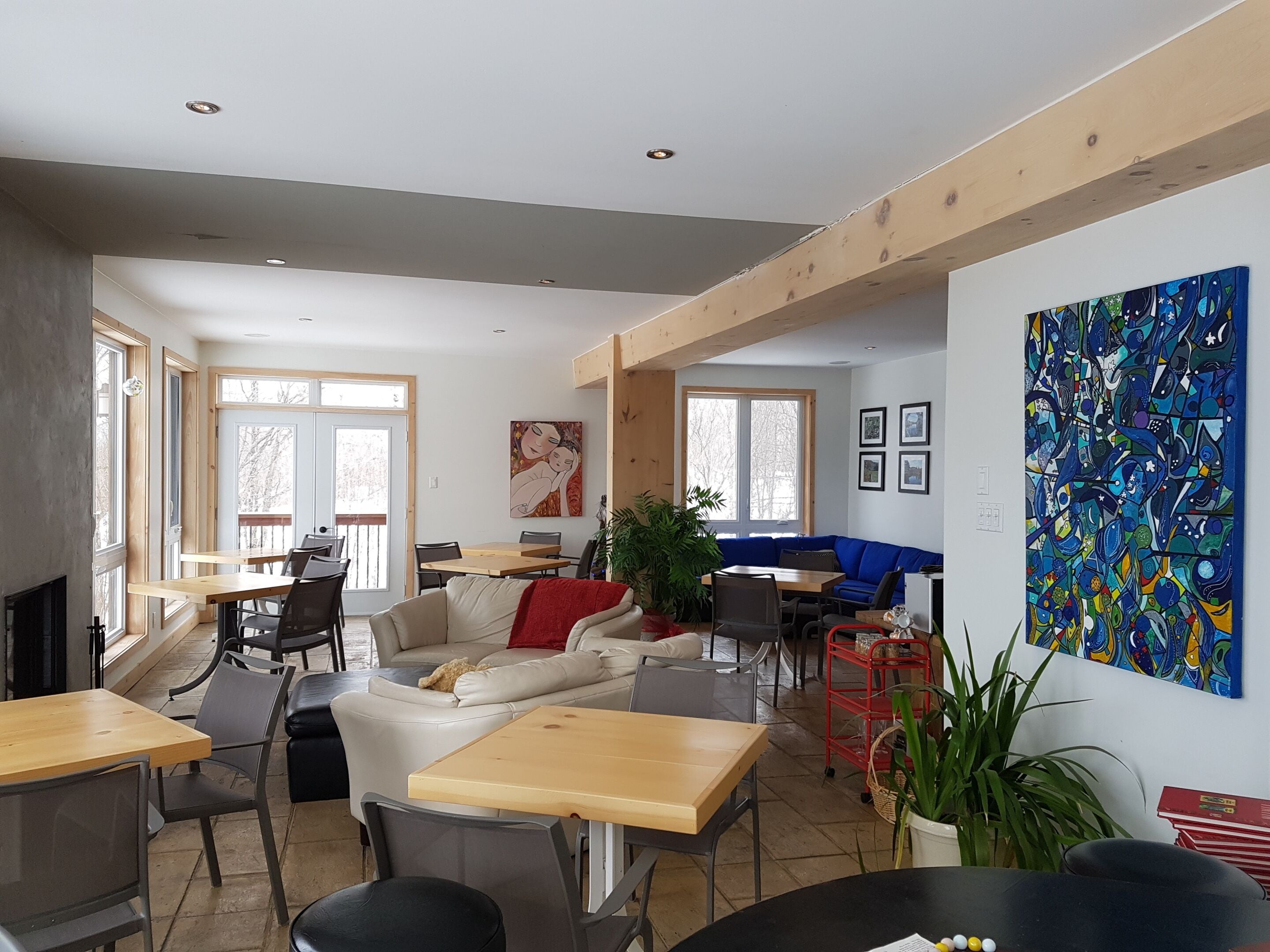 Een ruime woonkamer met een bank, eettafel en stoelen. Er zijn grote ramen, een open haard en een schilderij aan de muur.