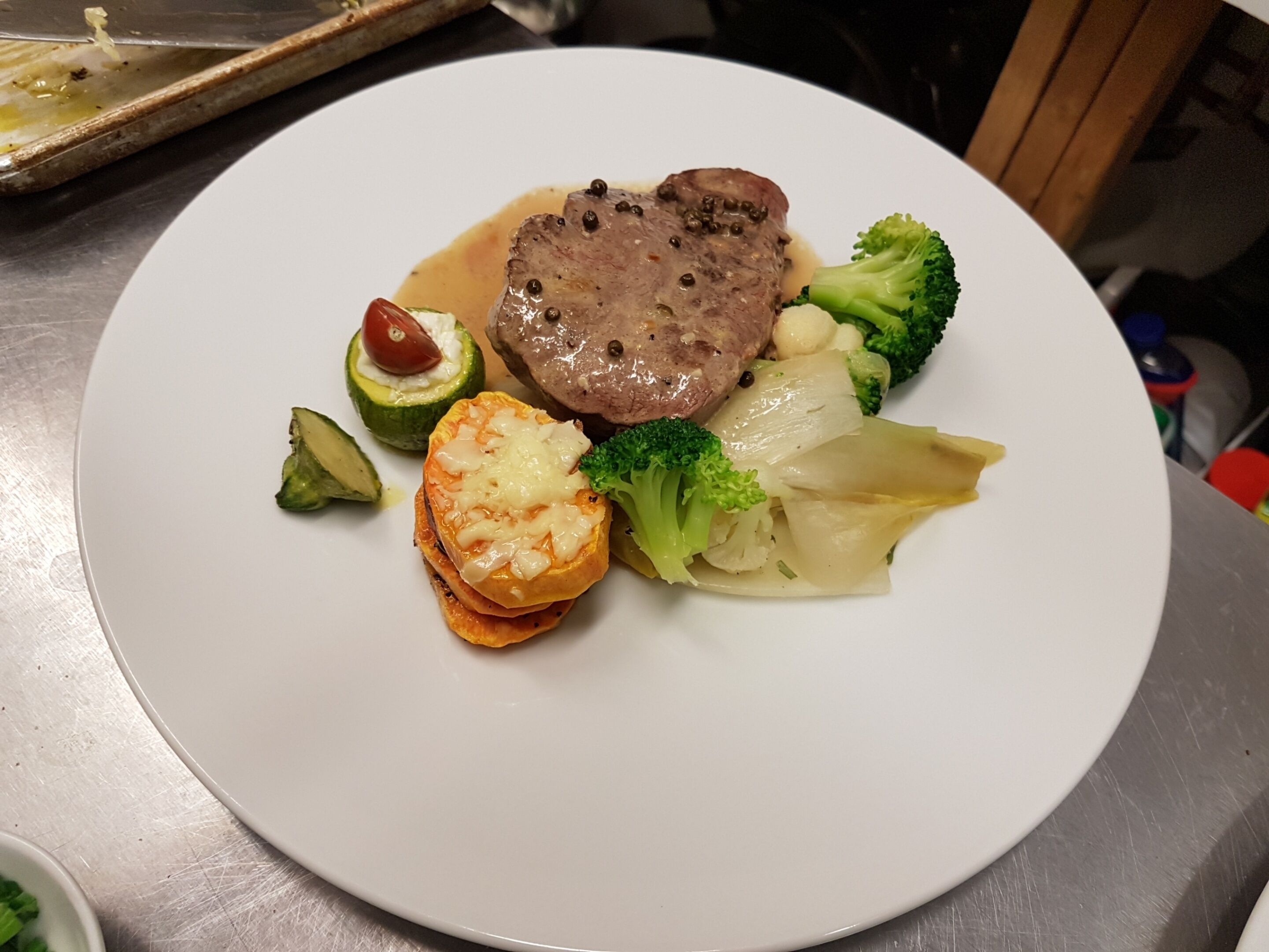 A plate of food with a steak, broccoli, and a small baked vegetable.
