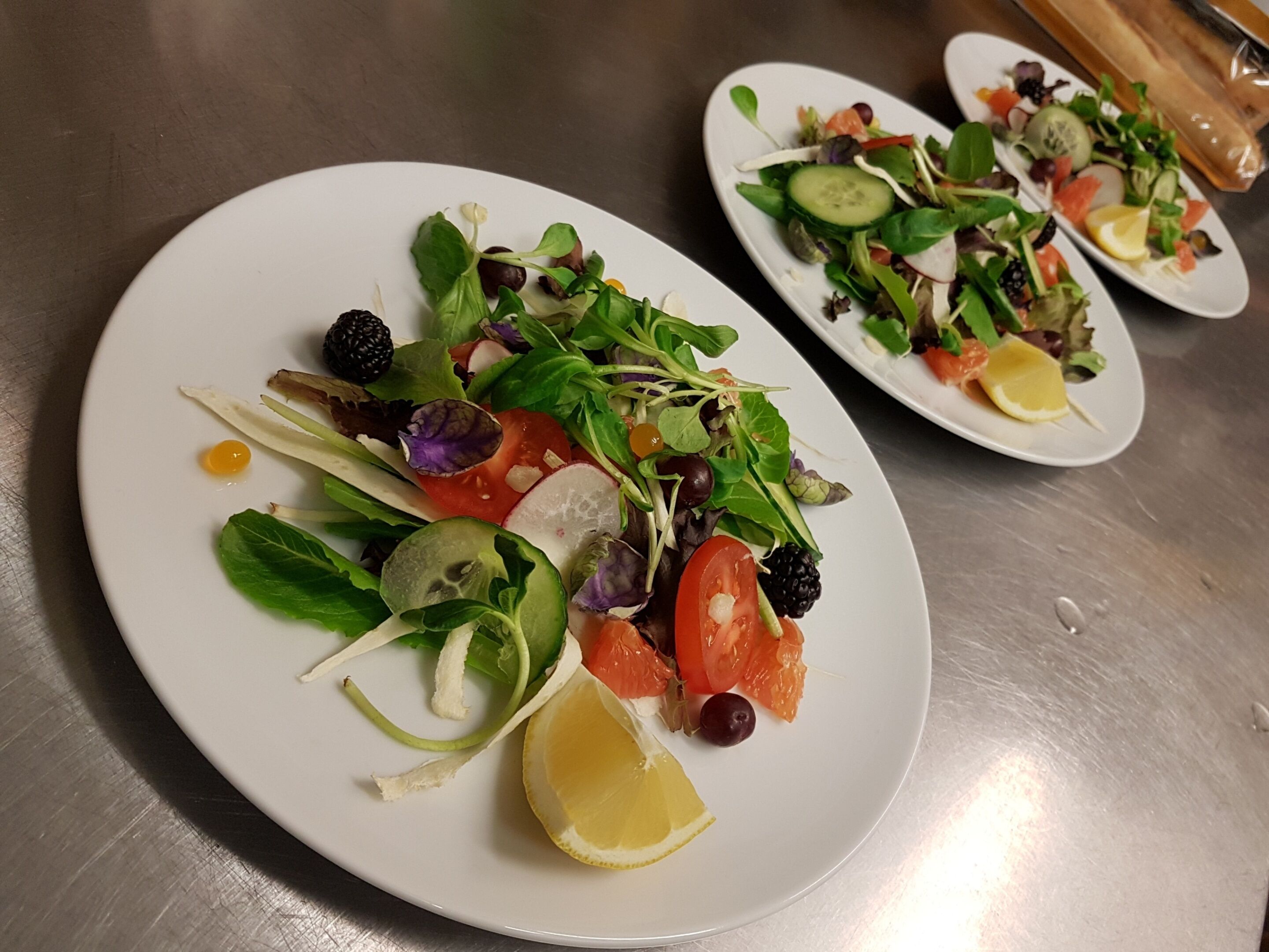 Un plato blanco con una ensalada que lleva varios vegetales y un gajo de limón.