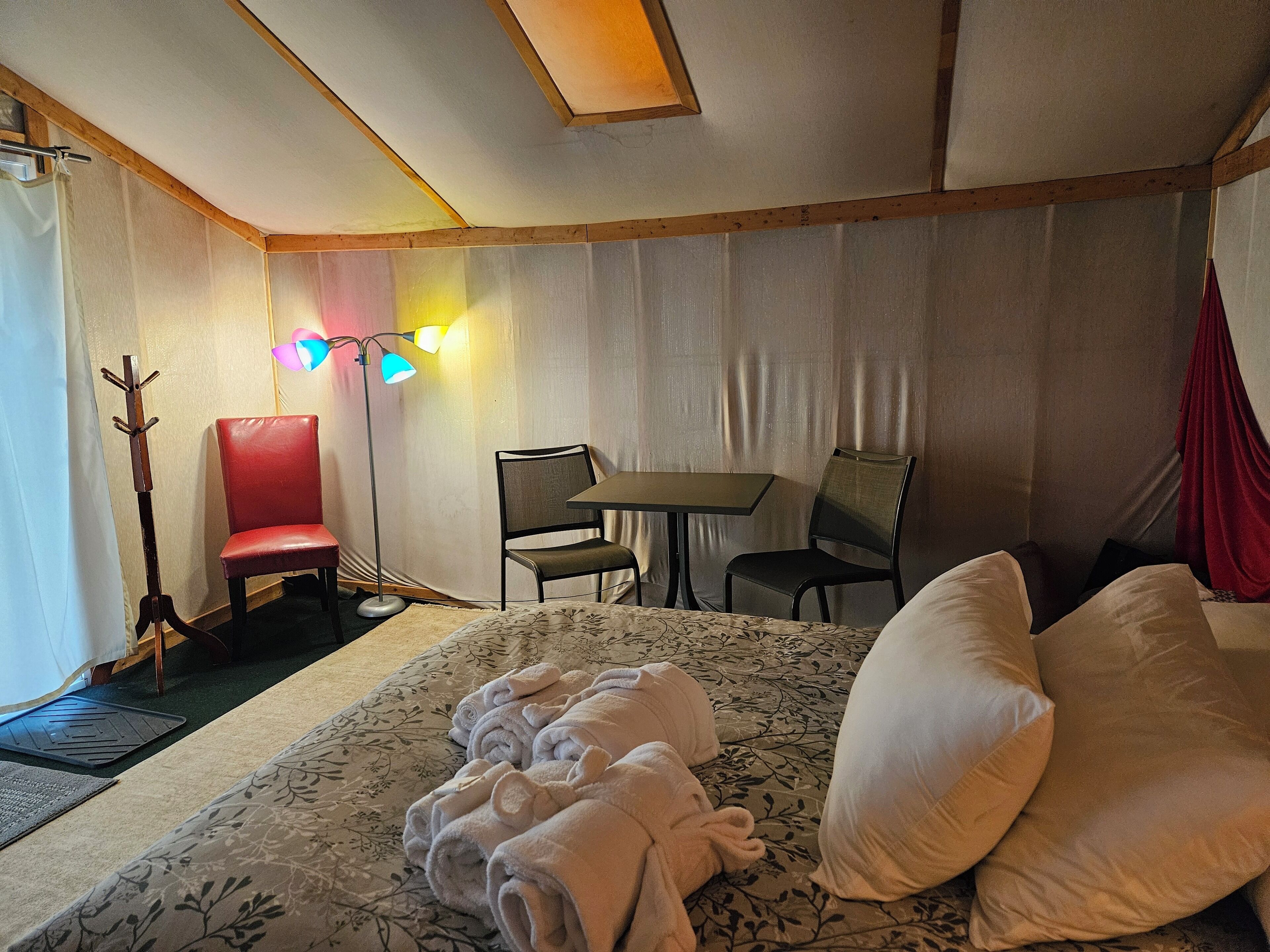 Una habitación de hotel con una cama, dos sillas, una mesa y una lámpara de pie.