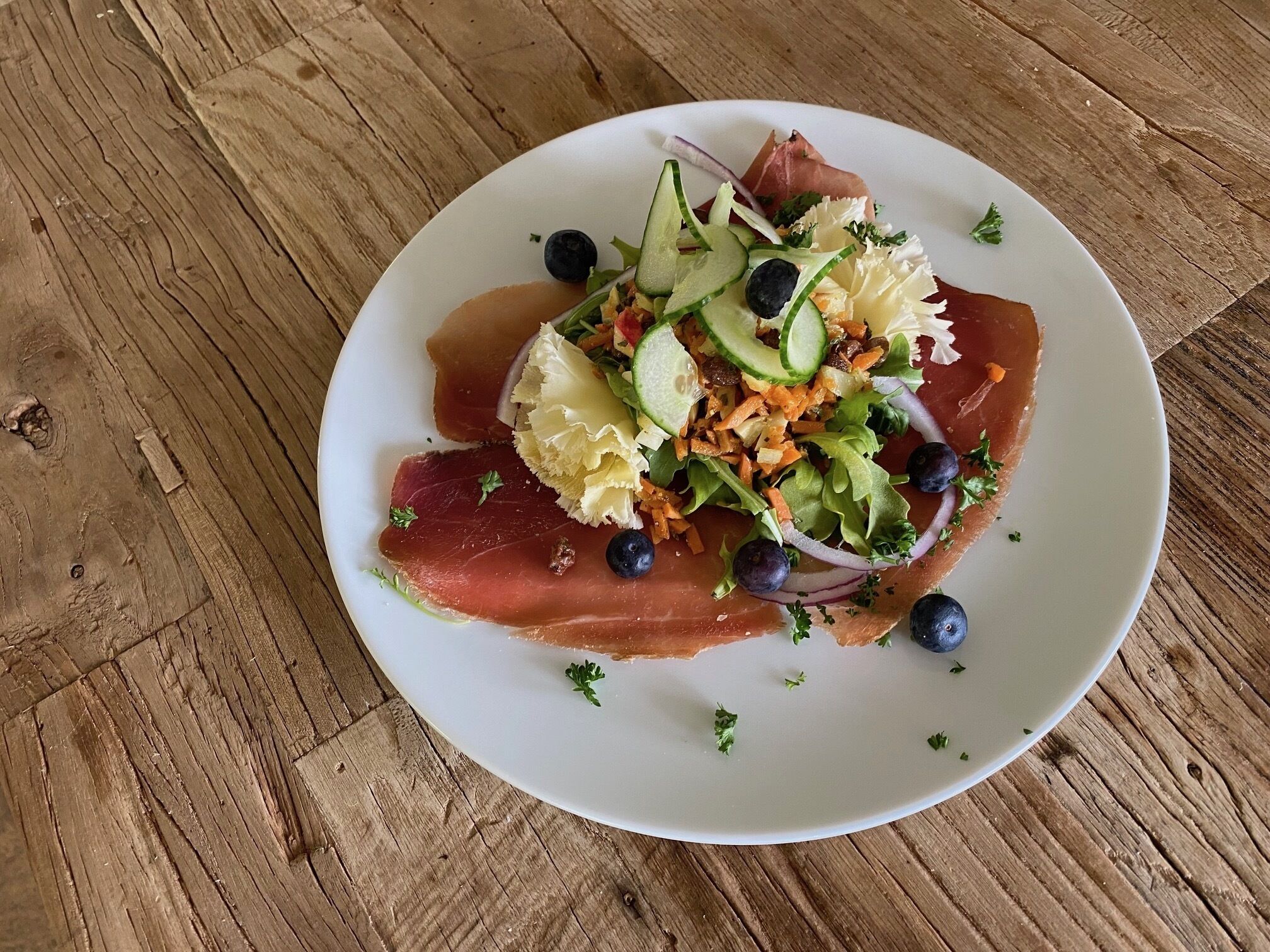 Une assiette de nourriture contenant de la viande en tranches, des légumes et des accompagnements, posée sur une table en bois.