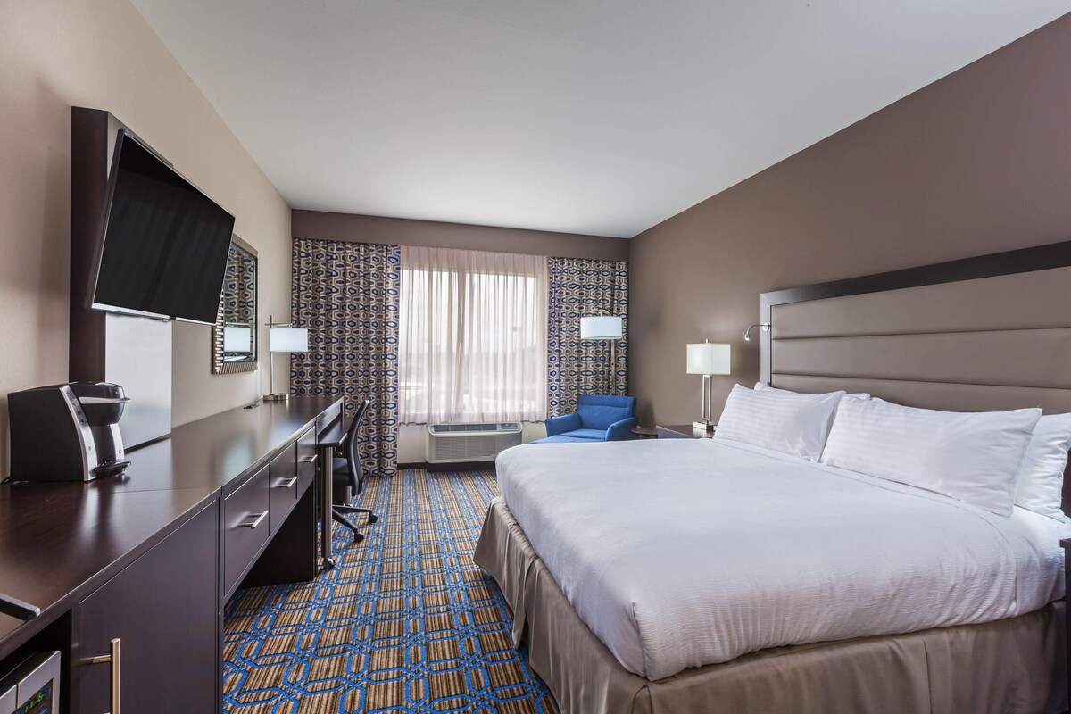 A hotel room with a bed, desk, chair, TV, and air conditioning unit.