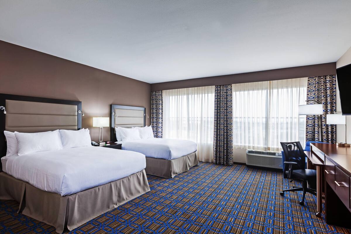 A hotel room with two beds, a desk, a chair, a TV, and a window with curtains.