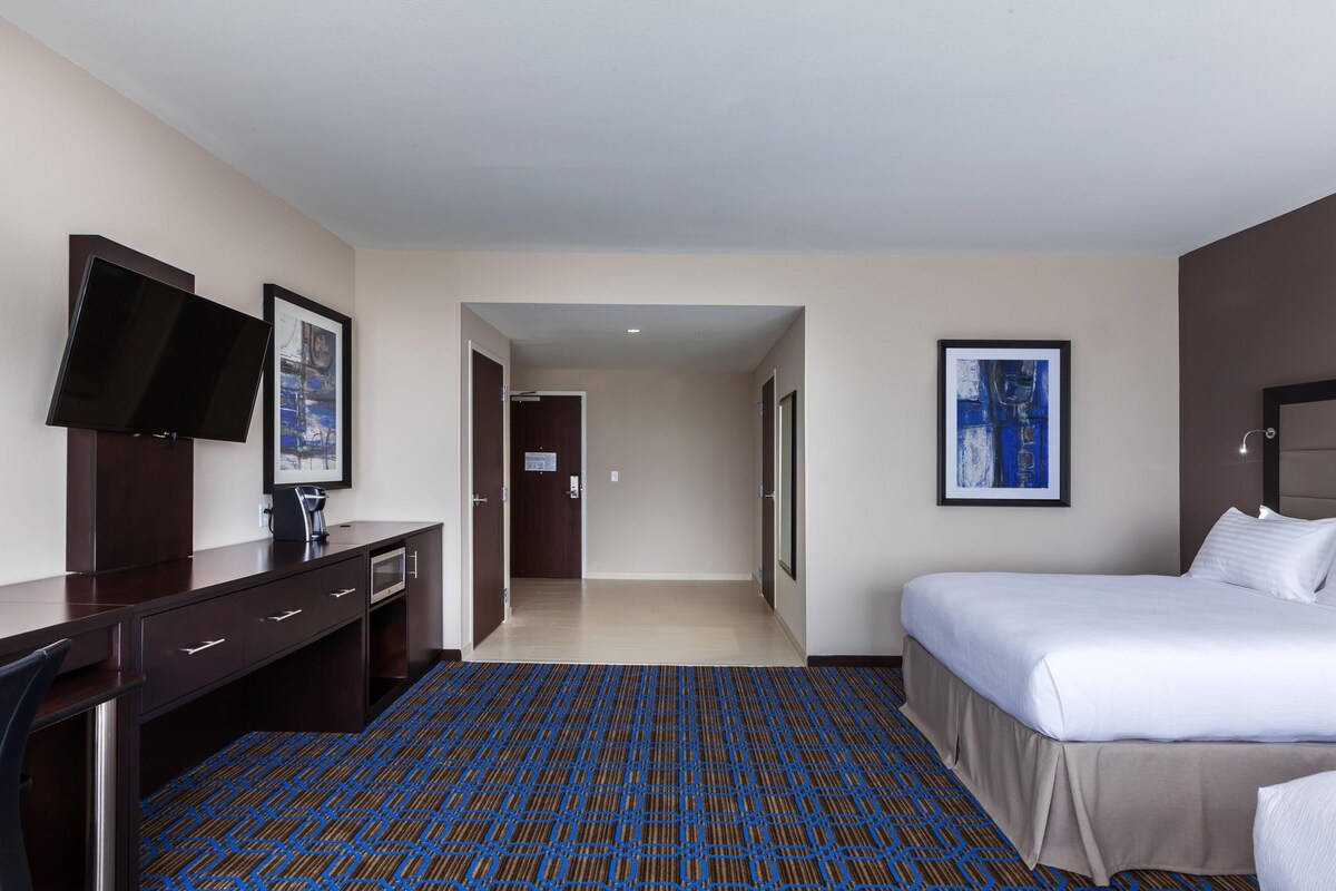A hotel room with a bed, a desk, a television, and a framed picture on the wall.