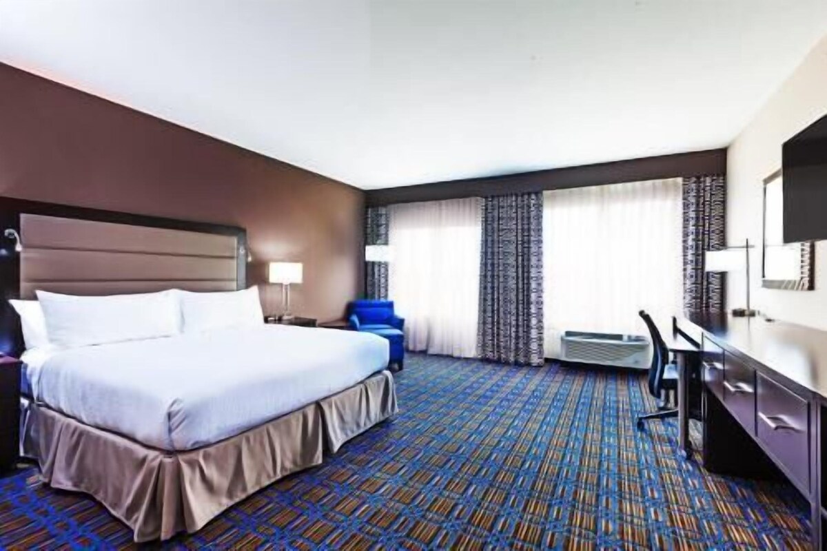 A hotel room with a large bed, a desk, a chair, and a television.