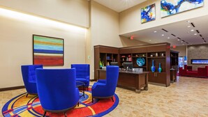 A hotel lobby with blue chairs, a desk with a computer, a fireplace, and artwork on the walls. - Clarion Hotel The Colony - Plano West (The Colony)