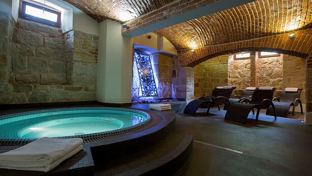 A spa area with a hot tub, stone walls, and a seating area with chairs. - Pałac Polanka (Krosno)