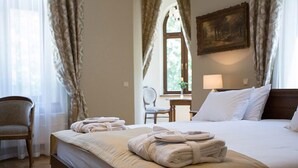 A neatly made bed with towels, a chair, a lamp, and a painting on the wall. - Pałac Polanka (Krosno)