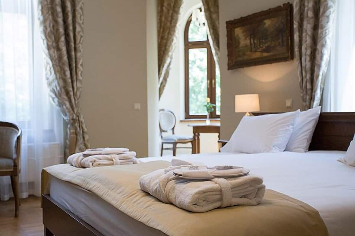 A neatly made bed with towels, a chair, a lamp, and a painting on the wall.