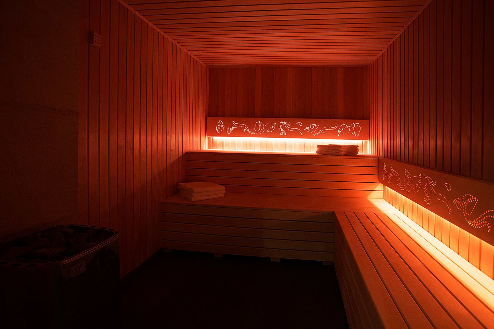 A sauna with wooden walls and benches, a bench with towels, and a wall-mounted light fixture.