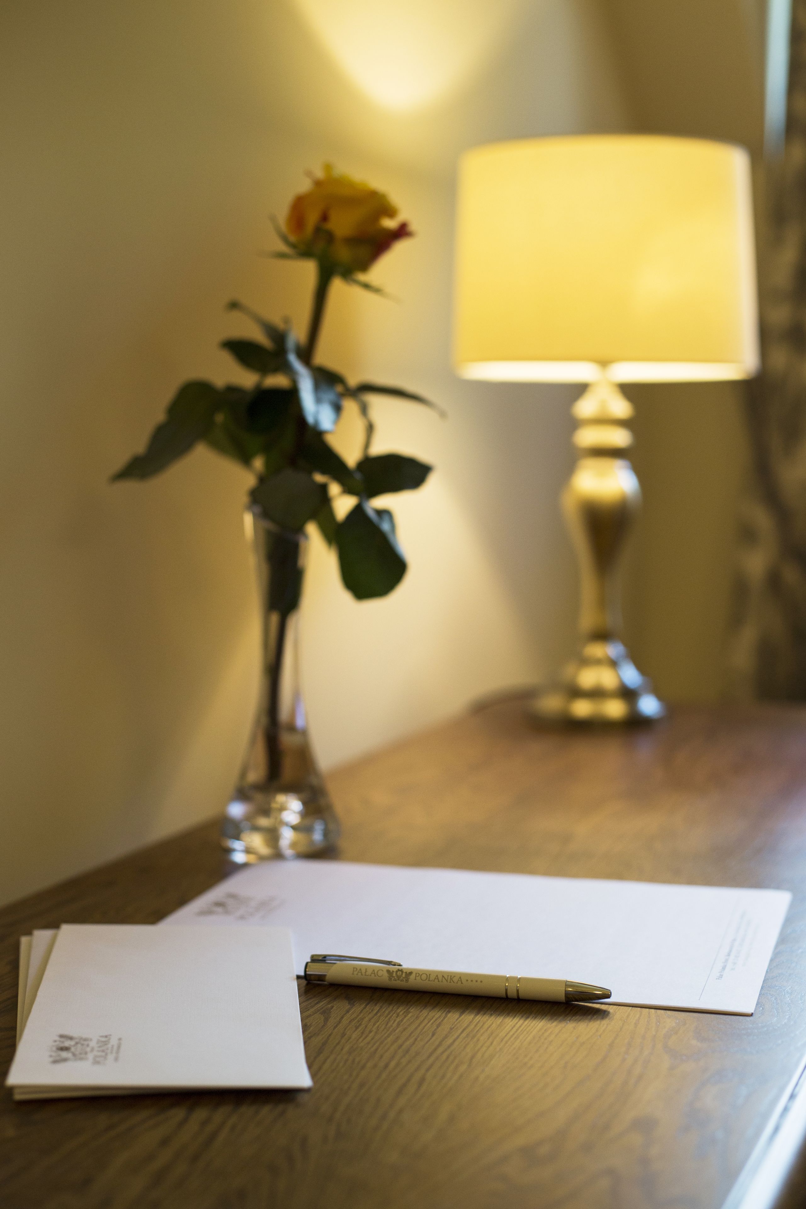 Een houten tafel met een vaas met een enkele gele roos, een pen en een stuk papier.