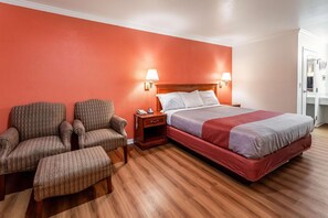 Una habitación de hotel con una cama, dos sillones, una mesita de noche y piso de madera.