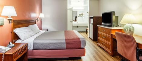 Habitación de hotel con cama, mesita de noche con teléfono, escritorio con televisor y espejo.