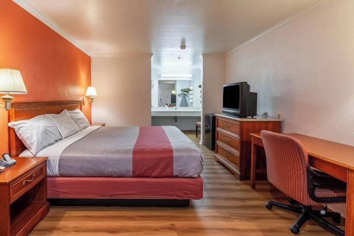 Habitación de hotel con cama, escritorio, televisor y cómoda.