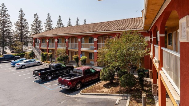 A motel with a red exterior, multiple balconies, and a parking lot with several vehicles. - Motel 6 Stockton Ca East (Stockton)