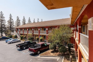 Un motel con fachada roja, varios balcones y un estacionamiento con varios vehículos.