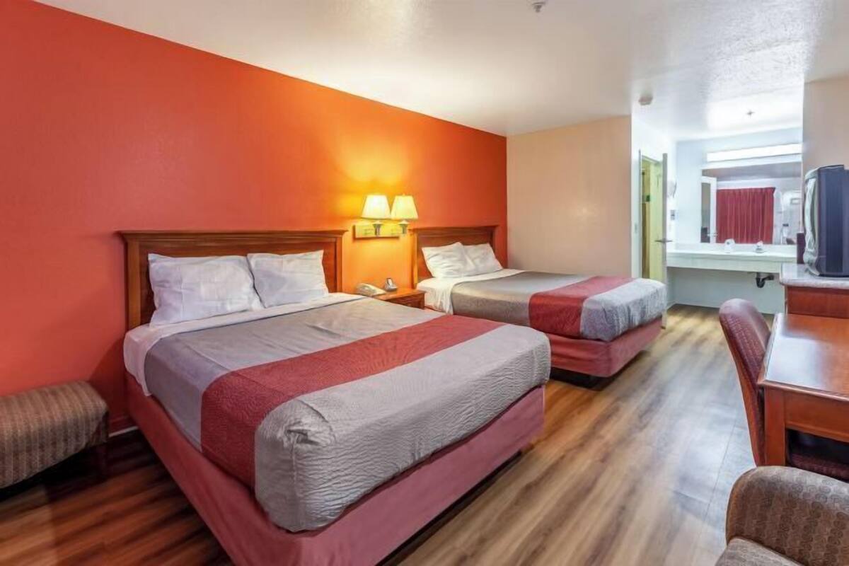 Una habitación de hotel con dos camas, suelo de madera, una mesita y una silla.