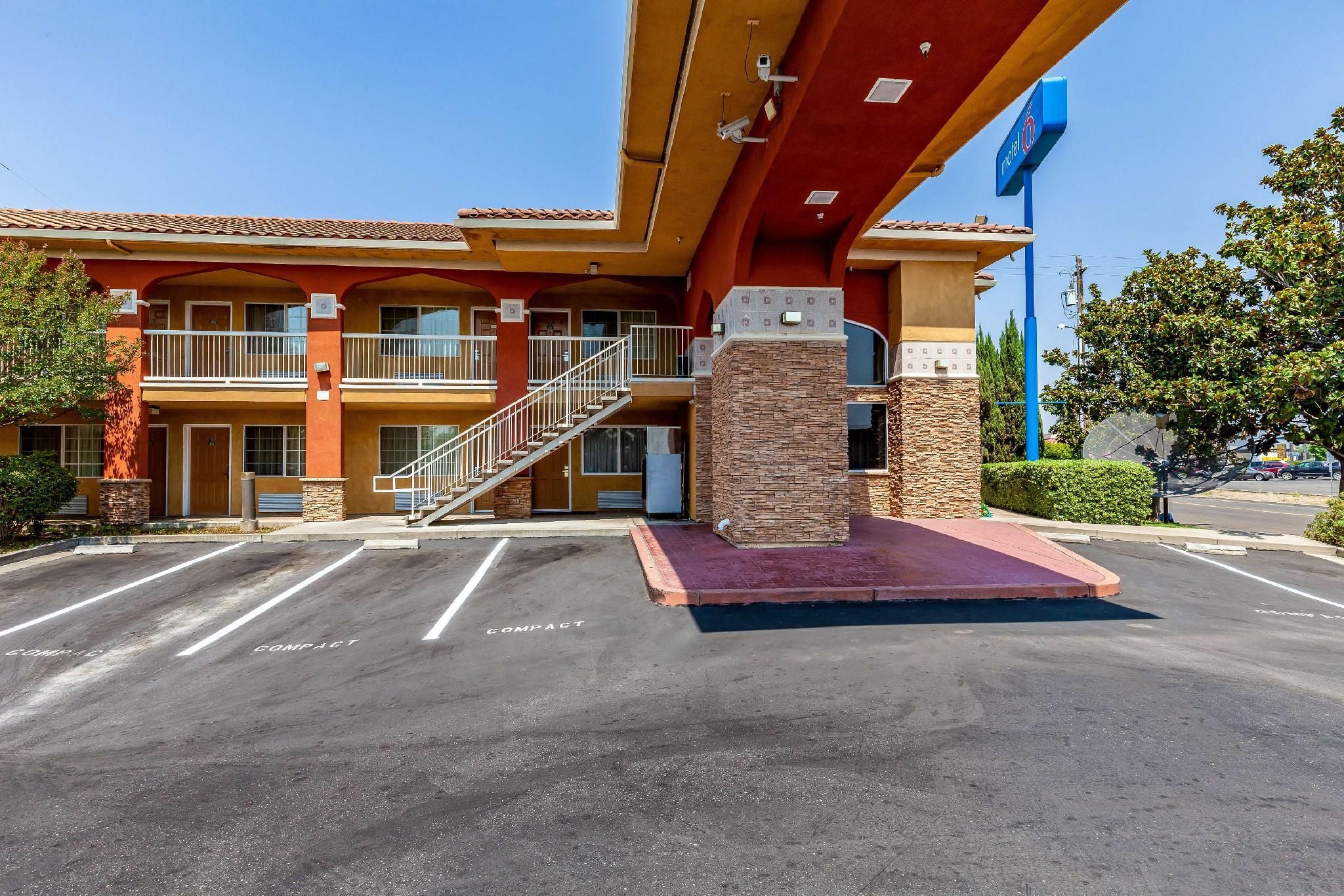 A hotel with a red and yellow facade, a staircase leading to the entrance, and a parking lot with compact parking spaces.