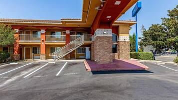 A hotel with a red and yellow facade, a staircase leading to the entrance, and a parking lot with compact parking spaces.