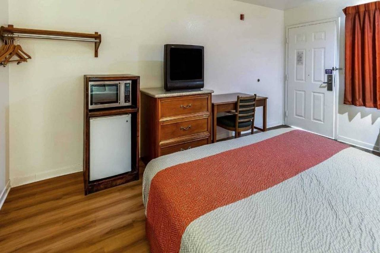 Una habitación de hotel con una cama, un escritorio con televisor, un microondas y un armario.