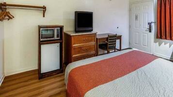 Una habitación de hotel con una cama, un escritorio con televisor, un microondas y un armario.