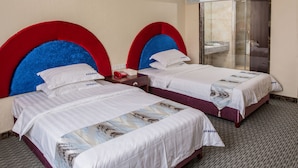Habitación de hotel con dos camas, cada una con cabecero rojo y azul, ropa de cama blanca y una mesita de noche pequeña con un teléfono rojo.