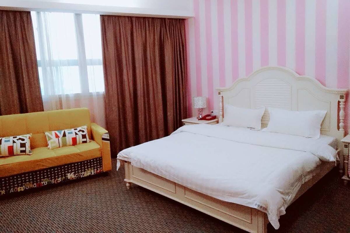 Habitación de hotel con una cama grande, un sofá y una ventana con cortinas.