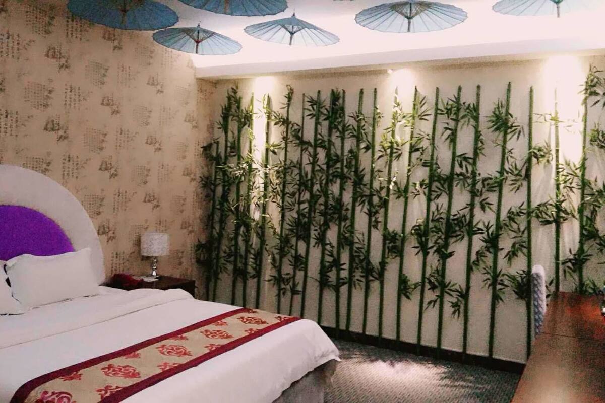 Habitación de hotel con una cama, una pared con plantas de bambú verticales y un techo con paraguas azules.