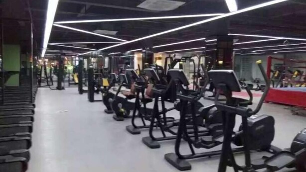 Un gimnasio con diversas máquinas de ejercicio, incluyendo cintas de correr y estaciones de pesas, dispuestas en filas.
