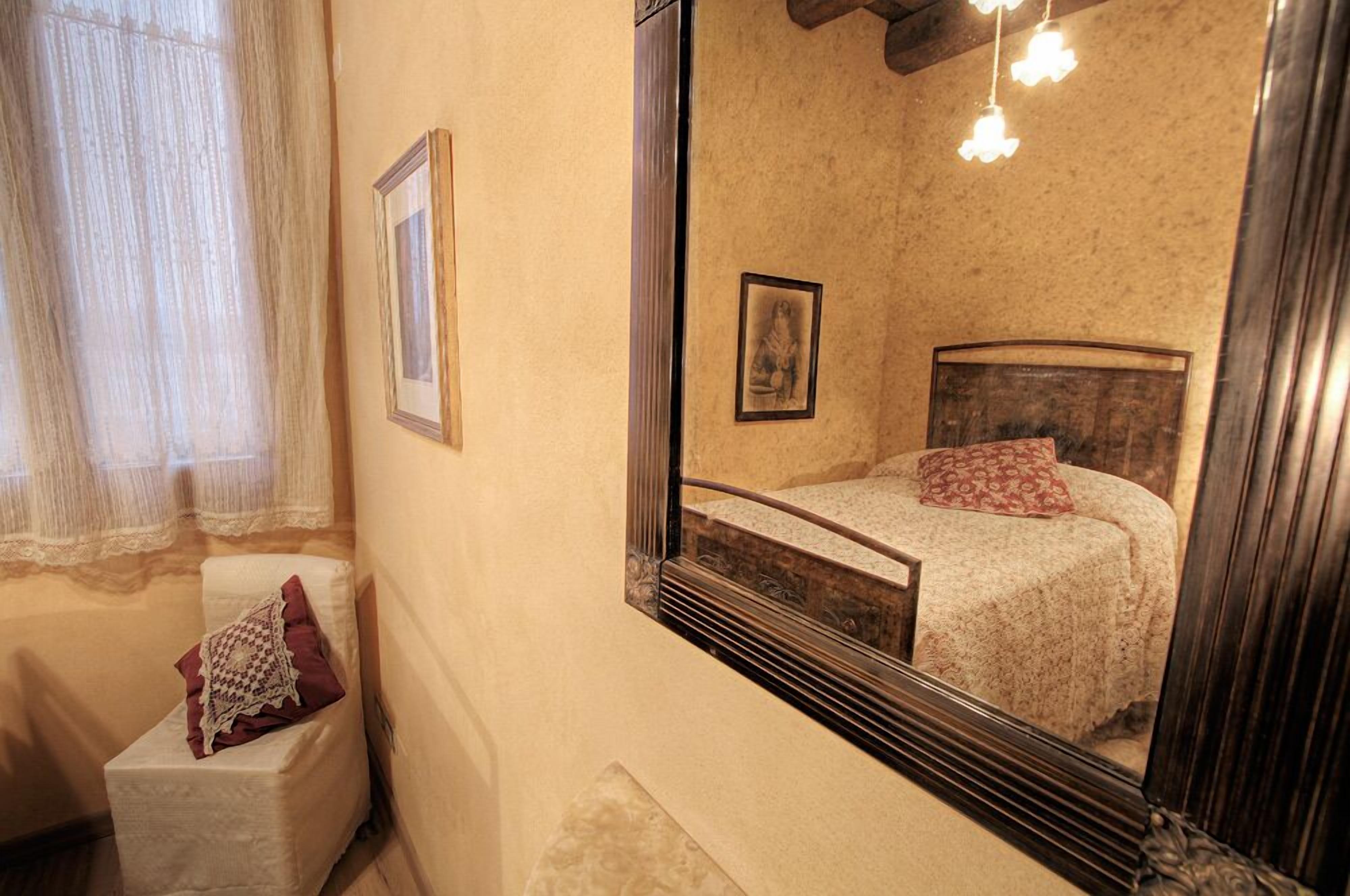 A bedroom with a bed, a chair, a mirror, and a window with curtains.