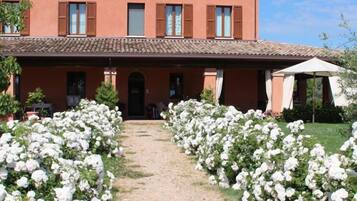 Un bâtiment à la façade rouge, doté d’un toit en tuiles et d’un chemin de gravier bordé de plantes à fleurs blanches.