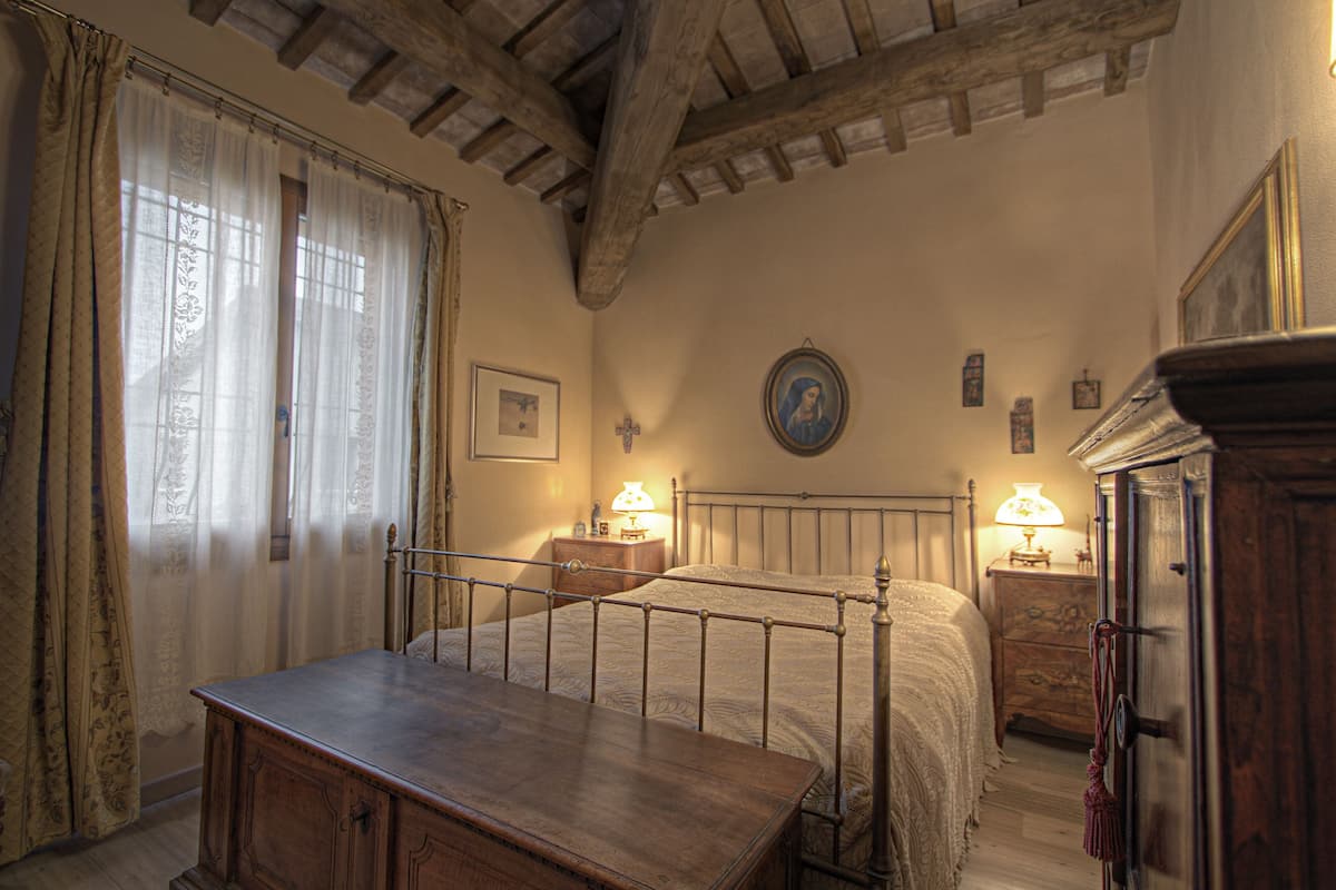 Une chambre à coucher avec un lit en bois, une table de chevet, une commode et une fenêtre avec des rideaux.