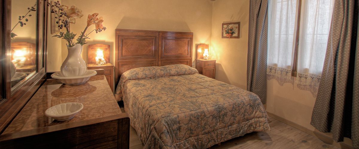 A bedroom with a bed, a nightstand, a vase with flowers, and a mirror.