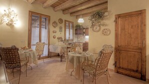 A dining area with wooden beams, a large wooden door, and a kitchen in the background. - La Fornasaccia (Cesena)