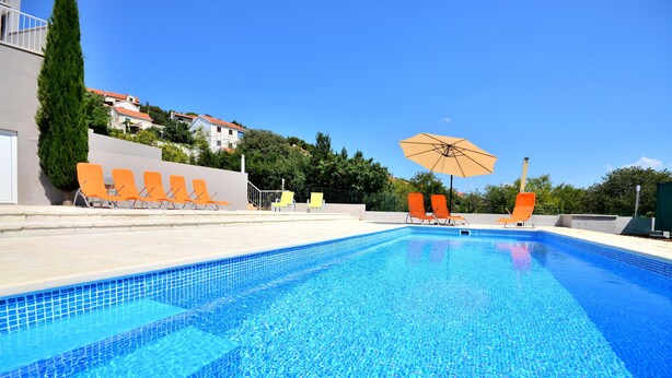 A swimming pool with clear blue water, surrounded by orange lounge chairs and a large umbrella. - BRETIA apartments & more (Sutivan)