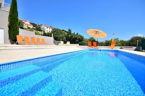 Una piscina con agua azul cristalina, rodeada de sillones naranja y un gran paraguas.