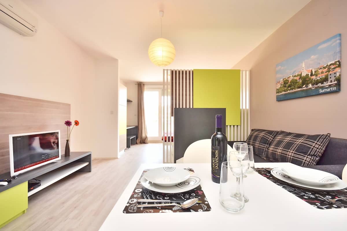 Una sala de estar moderna con una televisión de pantalla plana, una mesa de comedor con platos y cubiertos, una botella de vino y un sofá con un cojín escocés.
