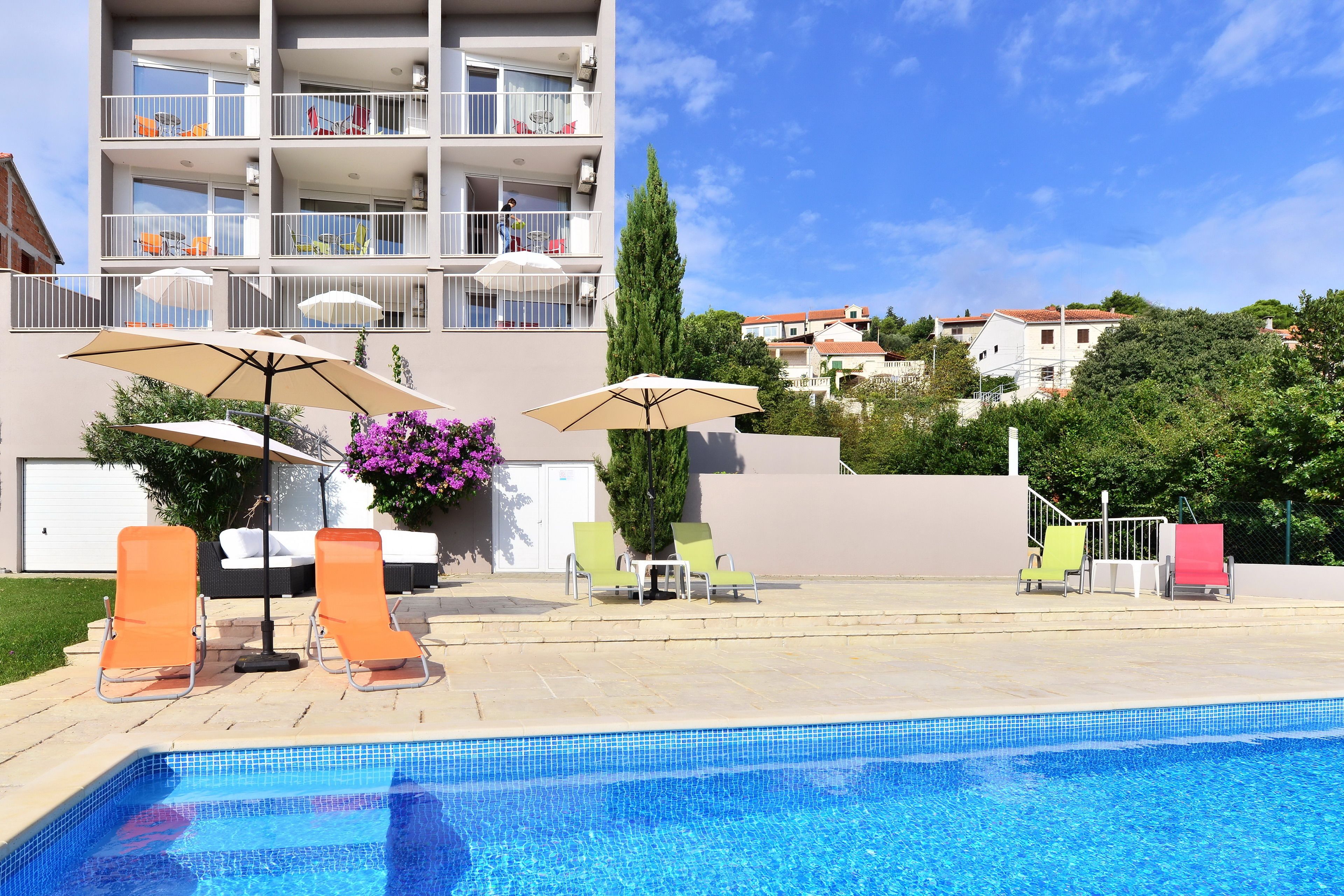Piscina com espreguiçadeiras e guarda-sóis, cercada por um edifício com varandas e céu claro.