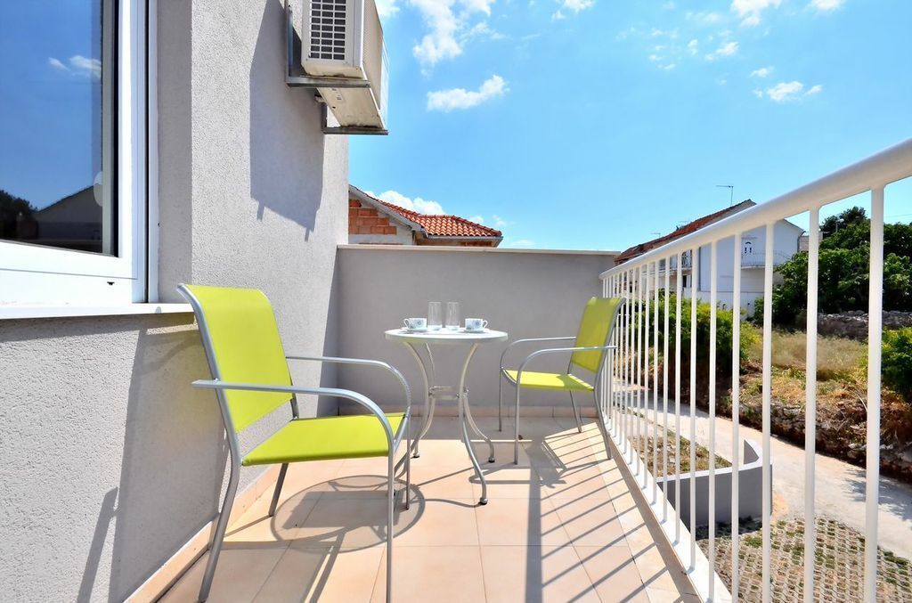 A balcony with two chairs and a small table, a white railing, and a view of a building with a red roof.