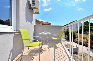 A balcony with two chairs and a small table, a white railing, and a view of a building with a red roof. - BRETIA apartments & more (Sutivan)