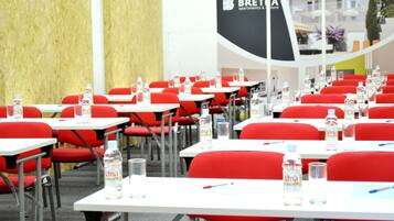 A conference room with red chairs and white tables, water bottles, and pens on each table.