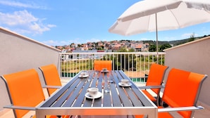 A balcony with a table set for four, orange chairs, and a white umbrella. - BRETIA apartments & more (Sutivan)